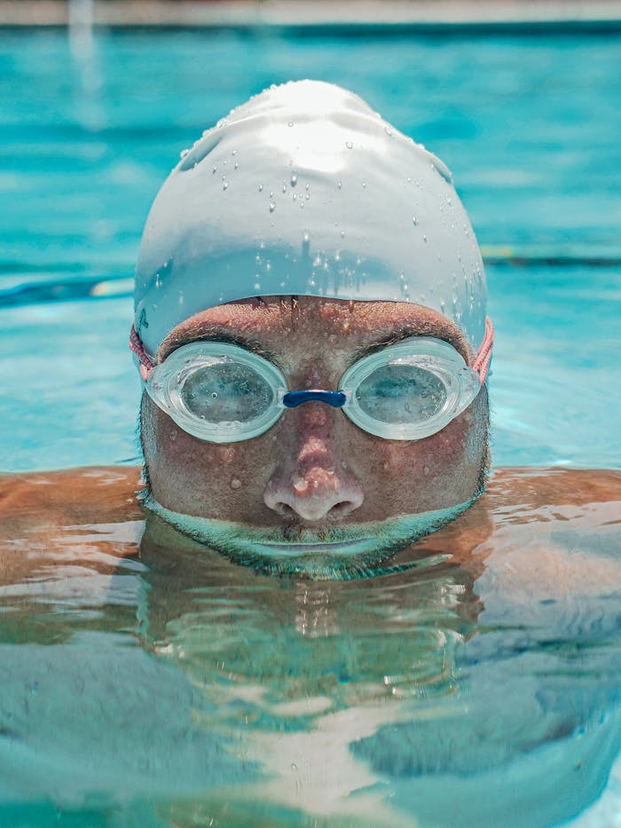 Close-up of a male swimmer in a pool wearing a swim cap and goggles, focused on training.