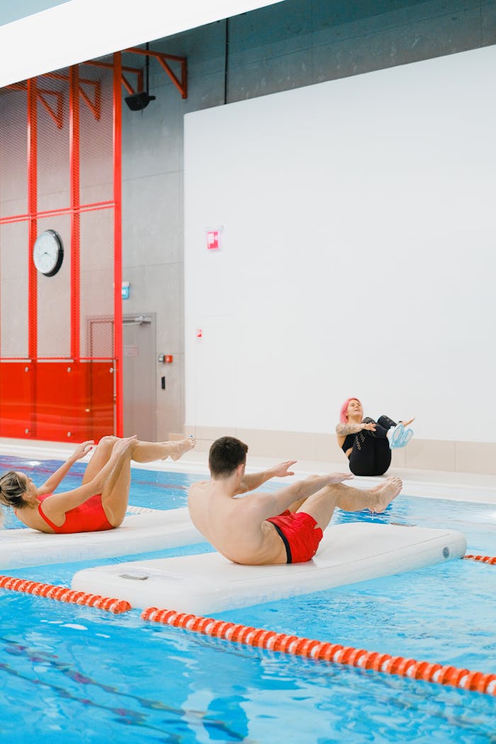 Participants engage in fitness exercises on flotation mats in an indoor swimming pool.